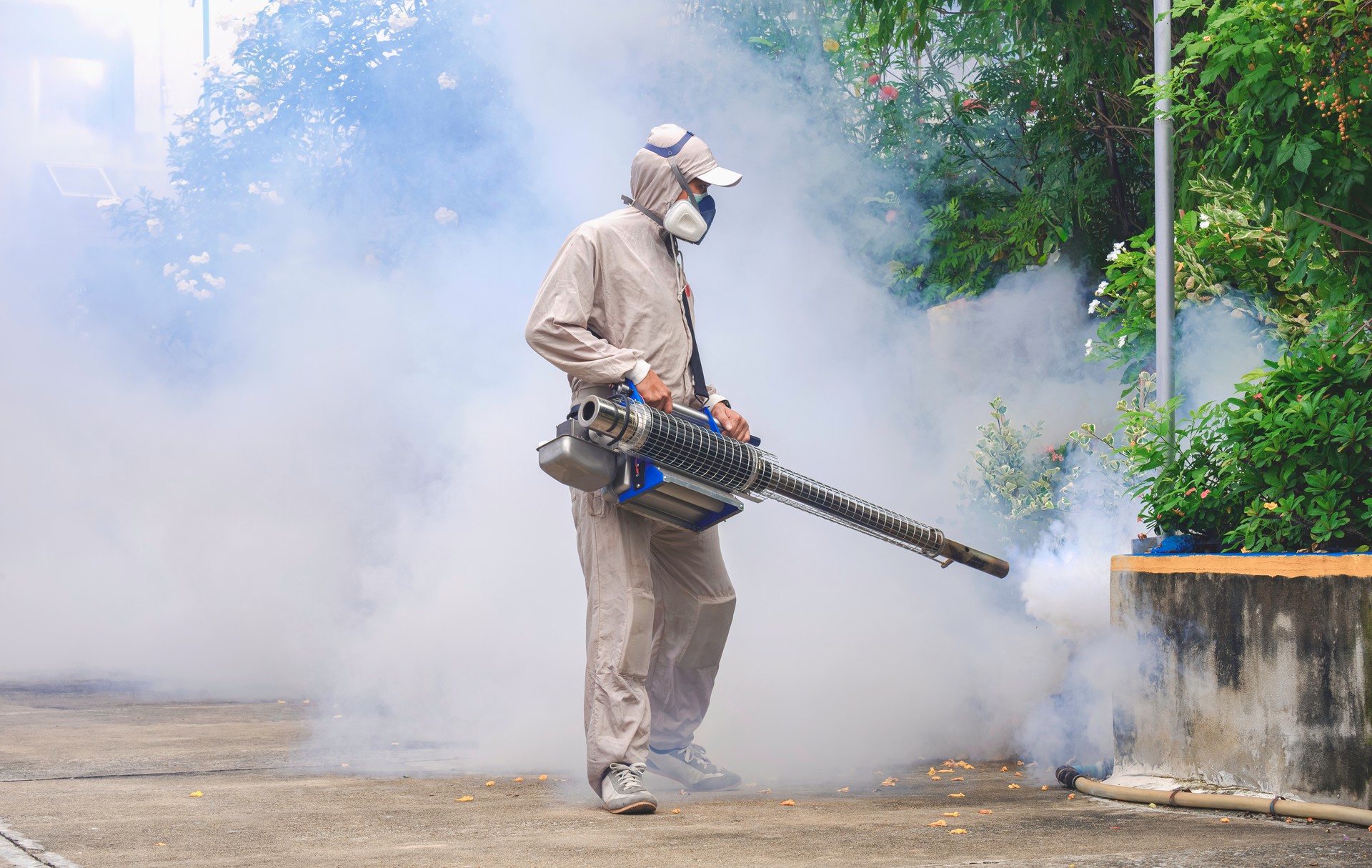 Outdoor healthcare worker spraying chemical to eliminate mosquitoes in overgrown area at general location in public area